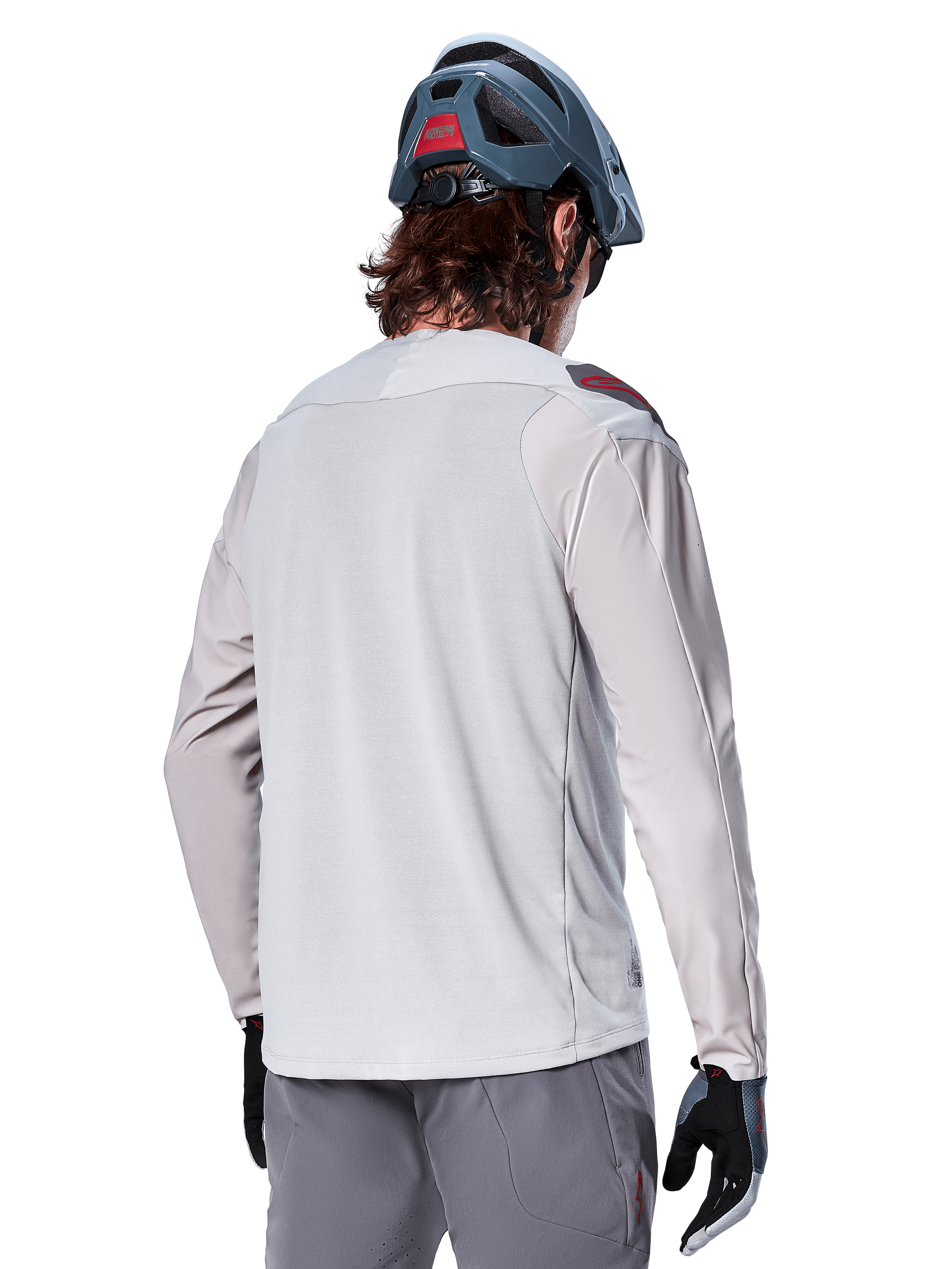 Alpinestars A-Aria Polartec Switch langærmet jersey, lysegrå, set bagfra på en rytter, båret med blå mountainbike-hjelm og grå bukser, funktionelt mountainbike-udstyr til terrænkørsel