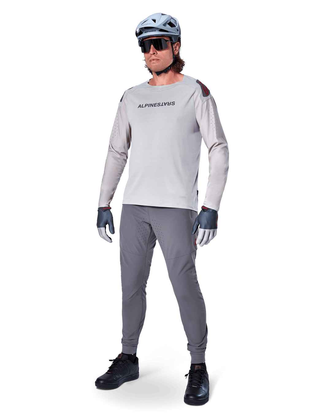 Alpinestars A-Aria Polartec Switch Jersey, langærmet MTB-trøje, lysegrå, båret med mørkegrå mountainbike-bukser, hjelm og handsker, med laserperforerede ærmer og Alpinestars-logo på brystet.