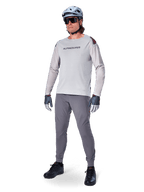 Alpinestars A-Aria Polartec Switch Jersey, langærmet MTB-trøje, lysegrå, båret med mørkegrå mountainbike-bukser, hjelm og handsker, med laserperforerede ærmer og Alpinestars-logo på brystet.