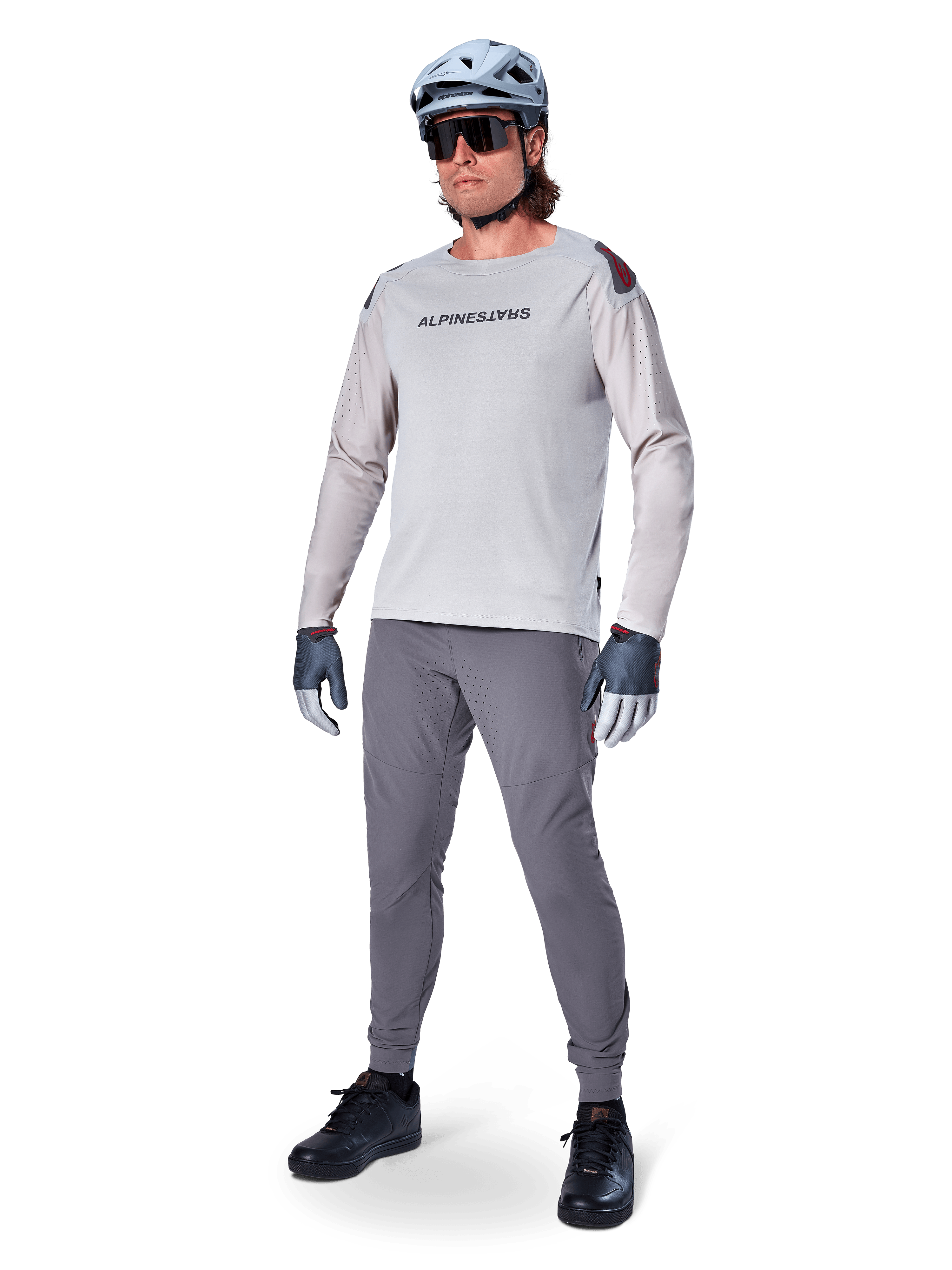 Alpinestars A-Aria Polartec Switch Jersey, langærmet MTB-trøje, lysegrå, båret med mørkegrå mountainbike-bukser, hjelm og handsker, med laserperforerede ærmer og Alpinestars-logo på brystet.