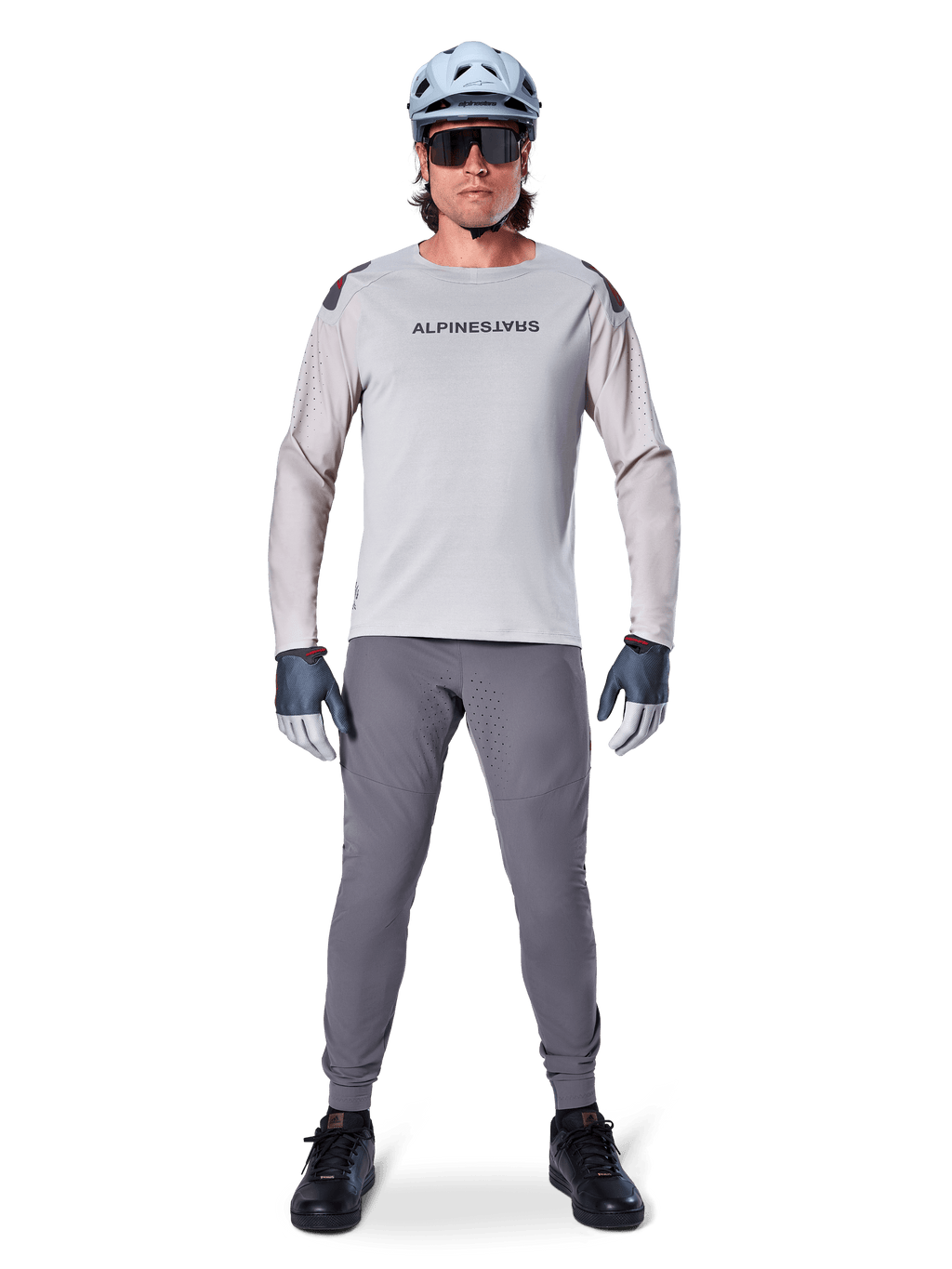 Alpinestars A-Aria Polartec Switch Jersey, langærmet, lysegrå, båret af en mandlig mountainbikerytter med mørkegrå MTB-bukser, lyseblå hjelm og solbriller, med branding på brystet og laserperforeret ventilation på ærmerne, komplet off-road køreudstyr.