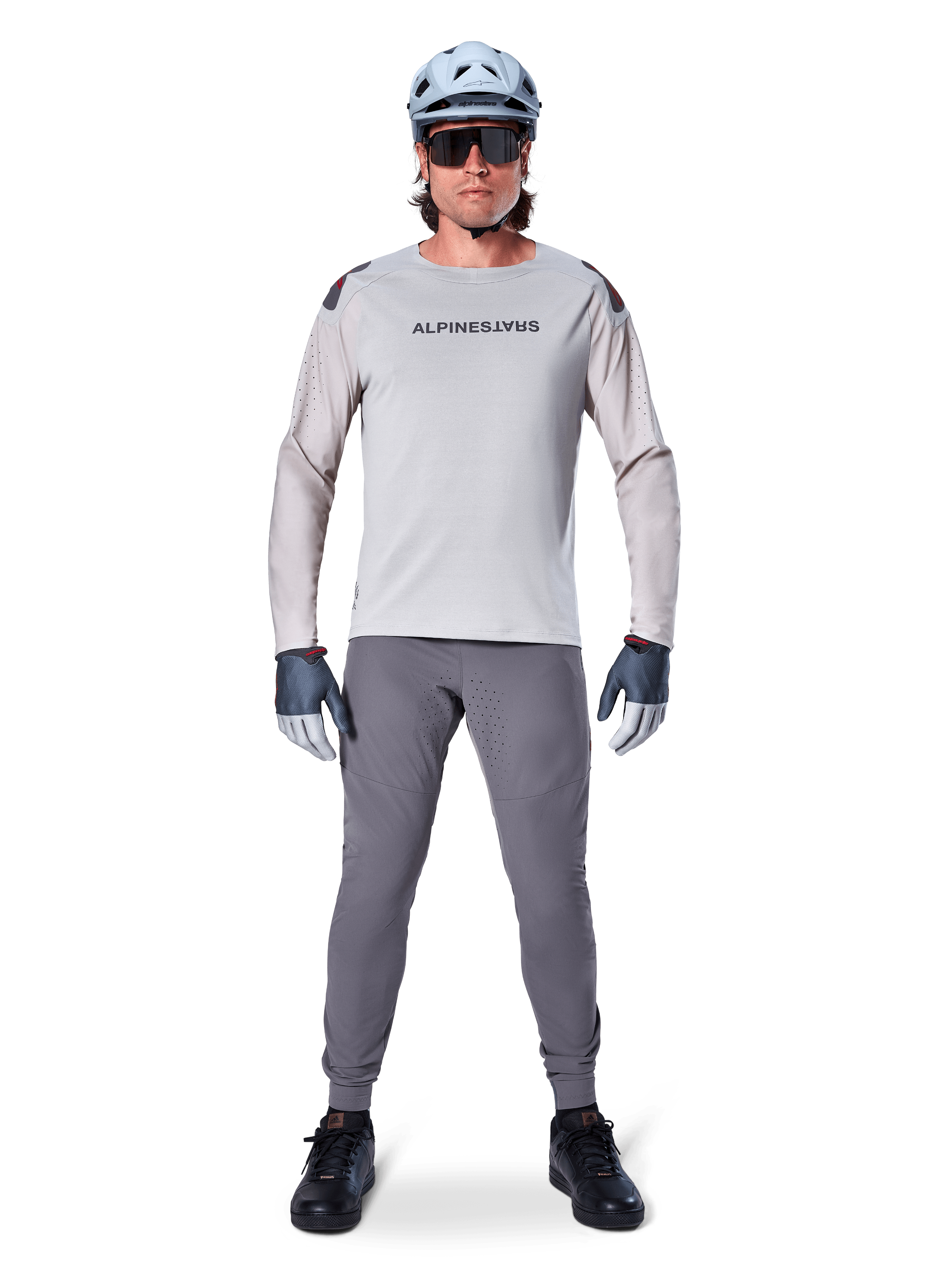 Alpinestars A-Aria Polartec Switch Jersey, langærmet, lysegrå, båret af en mandlig mountainbikerytter med mørkegrå MTB-bukser, lyseblå hjelm og solbriller, med branding på brystet og laserperforeret ventilation på ærmerne, komplet off-road køreudstyr.