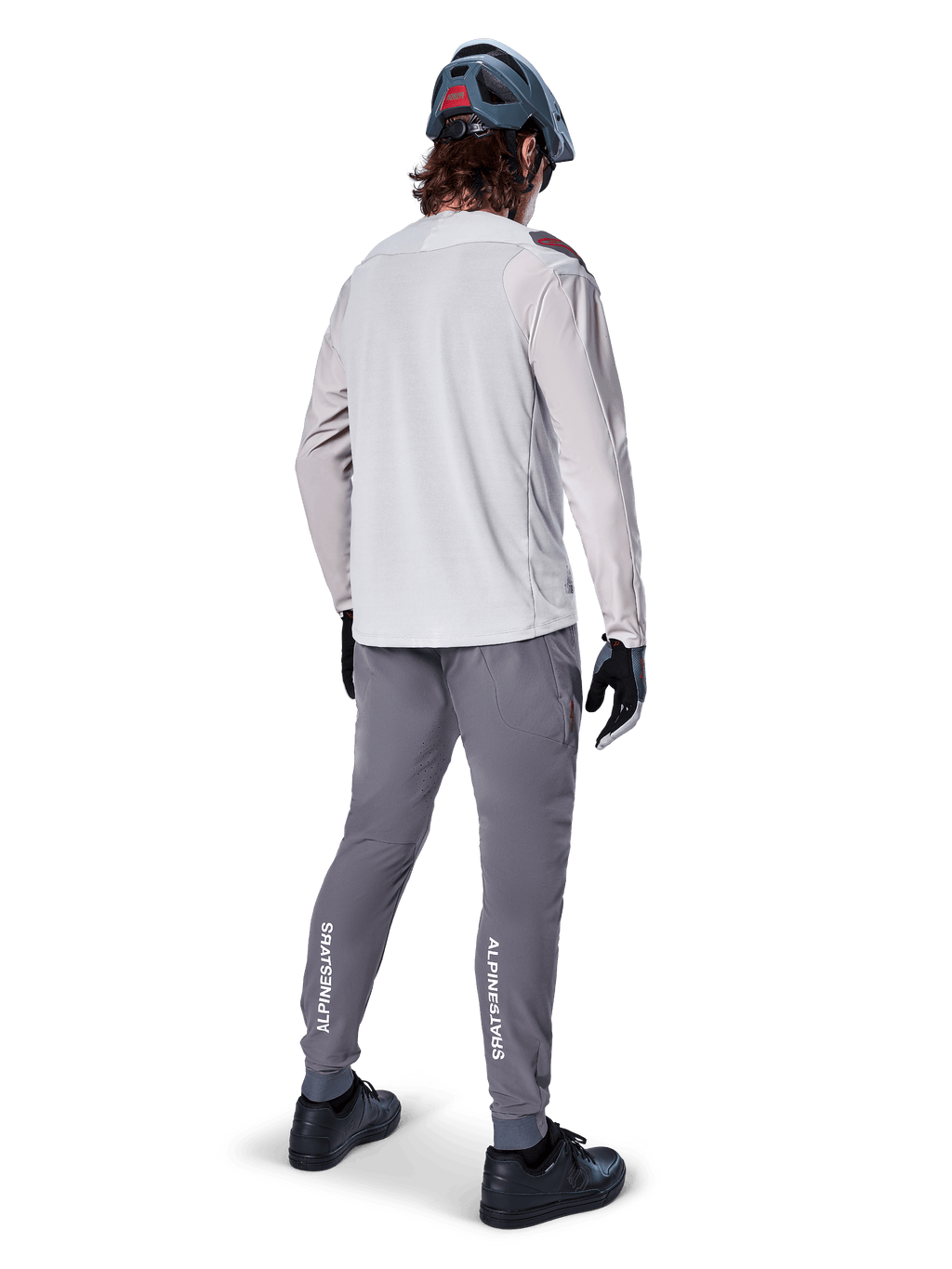 Set bagfra af en cyklist iført Alpinestars A-Aria Polartec Switch langærmet jersey i lysegrå, kombineret med mørkegrå mountainbikebukser med hvid Alpinestars-branding på læggene, sorte handsker og en grå hjelm.