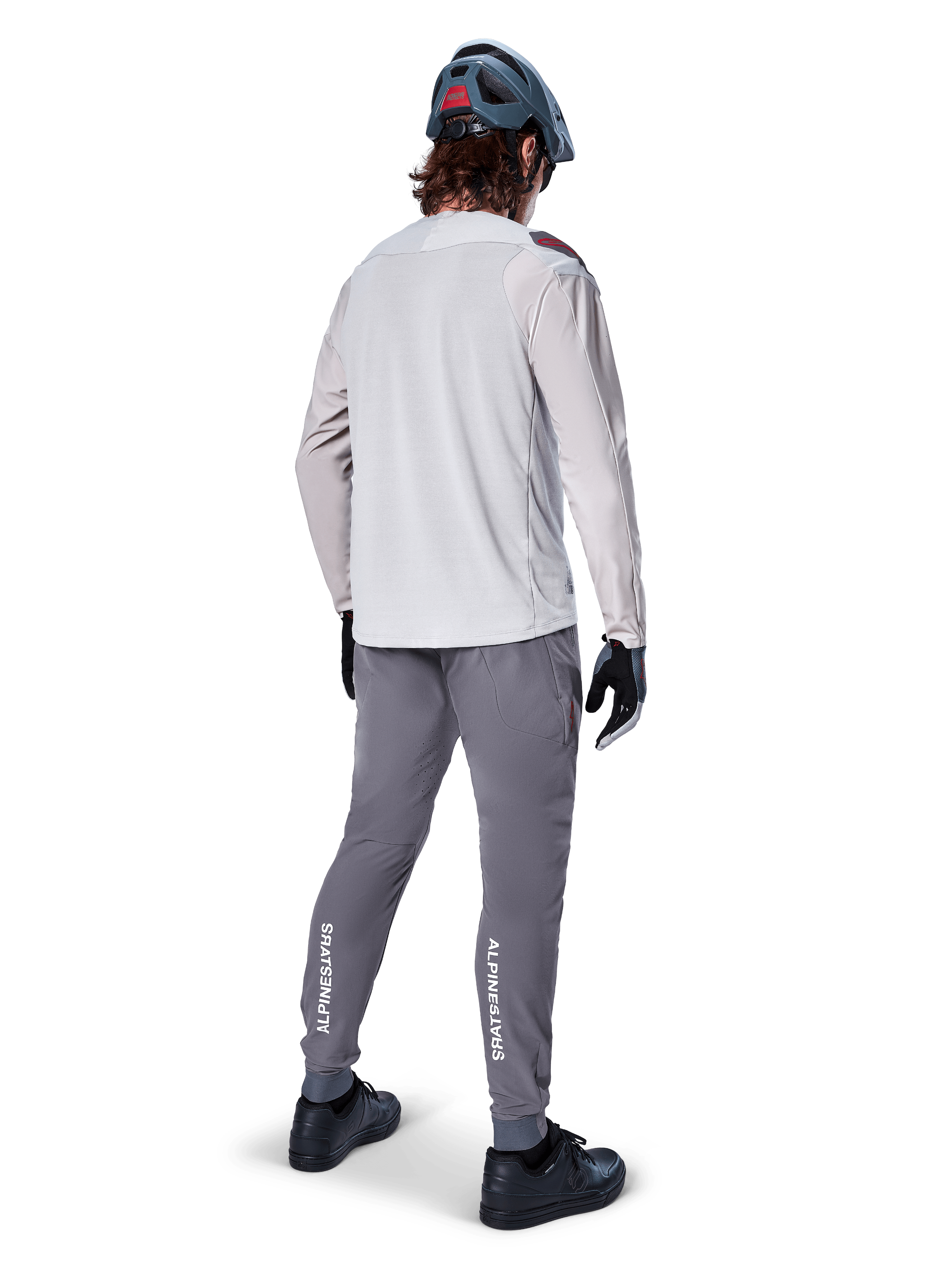 Set bagfra af en cyklist iført Alpinestars A-Aria Polartec Switch langærmet jersey i lysegrå, kombineret med mørkegrå mountainbikebukser med hvid Alpinestars-branding på læggene, sorte handsker og en grå hjelm.