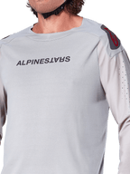 Nærbillede af Alpinestars A-Aria Polartec Switch langærmet jersey i lysegrå, med Alpinestars-branding på brystet, rødt skulderlogo og laserperforerede ærmer for luftgennemstrømning, premium mountainbike-udstyr