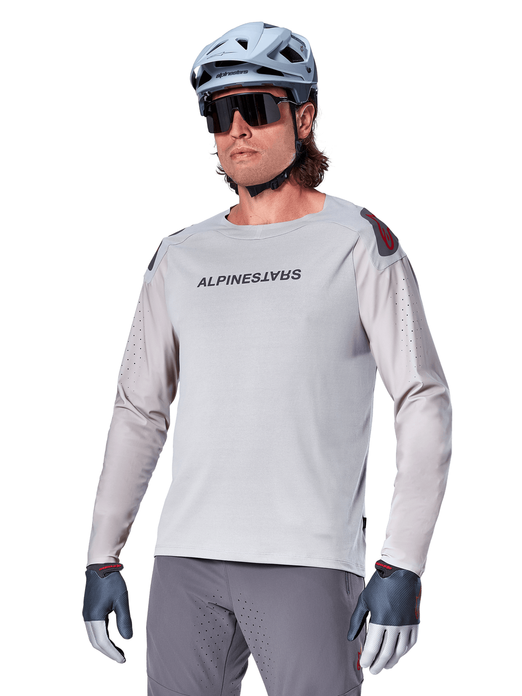 Alpinestars A-Aria Polartec Switch langærmet trøje, lysegrå cykeltrøje med sort brystlogo og røde skulderdetaljer, laserperforerede ærmer for ventilation, vist med lyseblå hjelm, solbriller og grå bukser, performance mountainbike-tøj til trail-kørsel