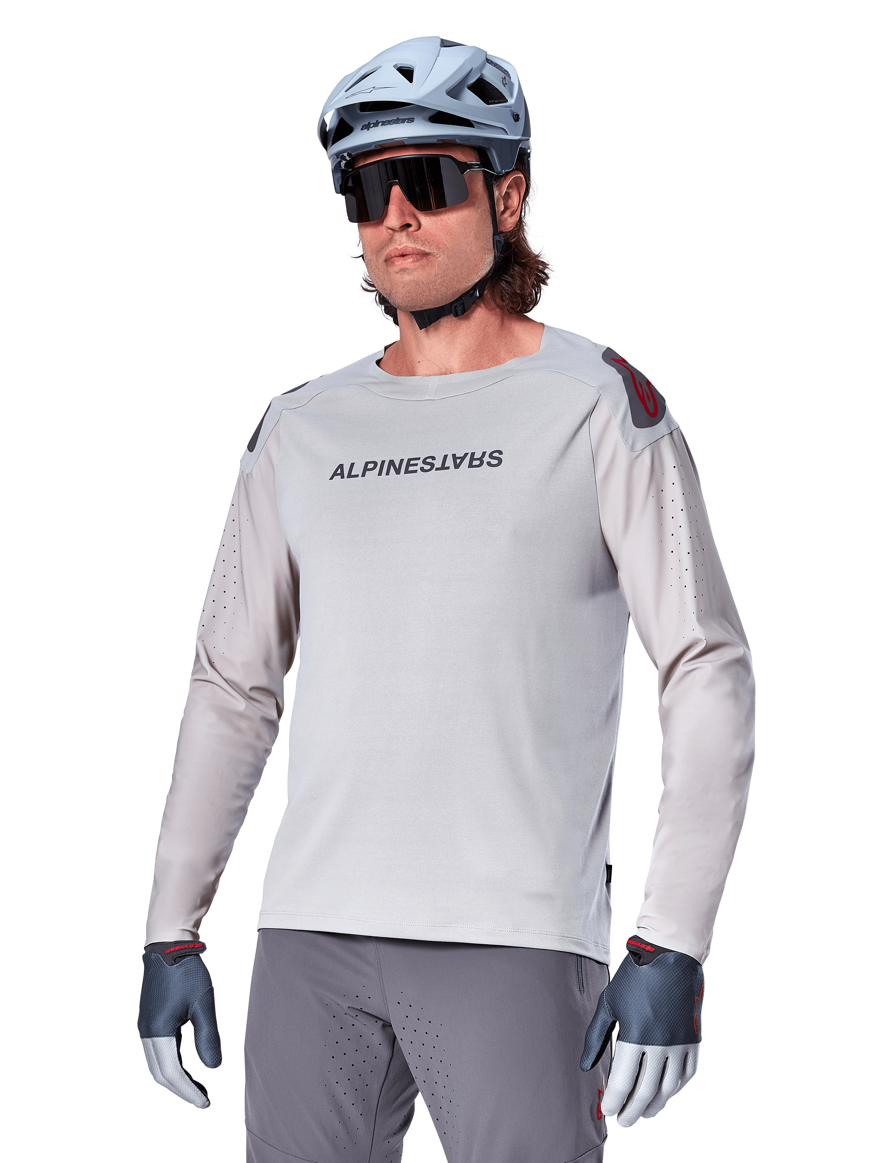 Alpinestars A-Aria Polartec Switch langærmet trøje, lysegrå cykeltrøje med sort brystlogo og røde skulderdetaljer, laserperforerede ærmer for ventilation, vist med lyseblå hjelm, solbriller og grå bukser, performance mountainbike-tøj til trail-kørsel