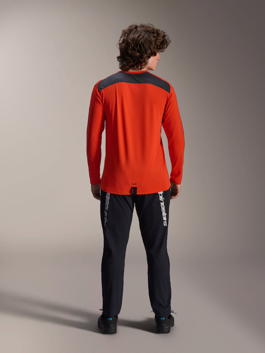 Alpinestars A-Dura Insert Astar langærmet trøje i Spicy Orange, set bagfra, koksgråt skulderpanel, kombineret med sorte Alpinestars bukser og sorte sko, professionelt studiebillede af MTB-performanceudstyr