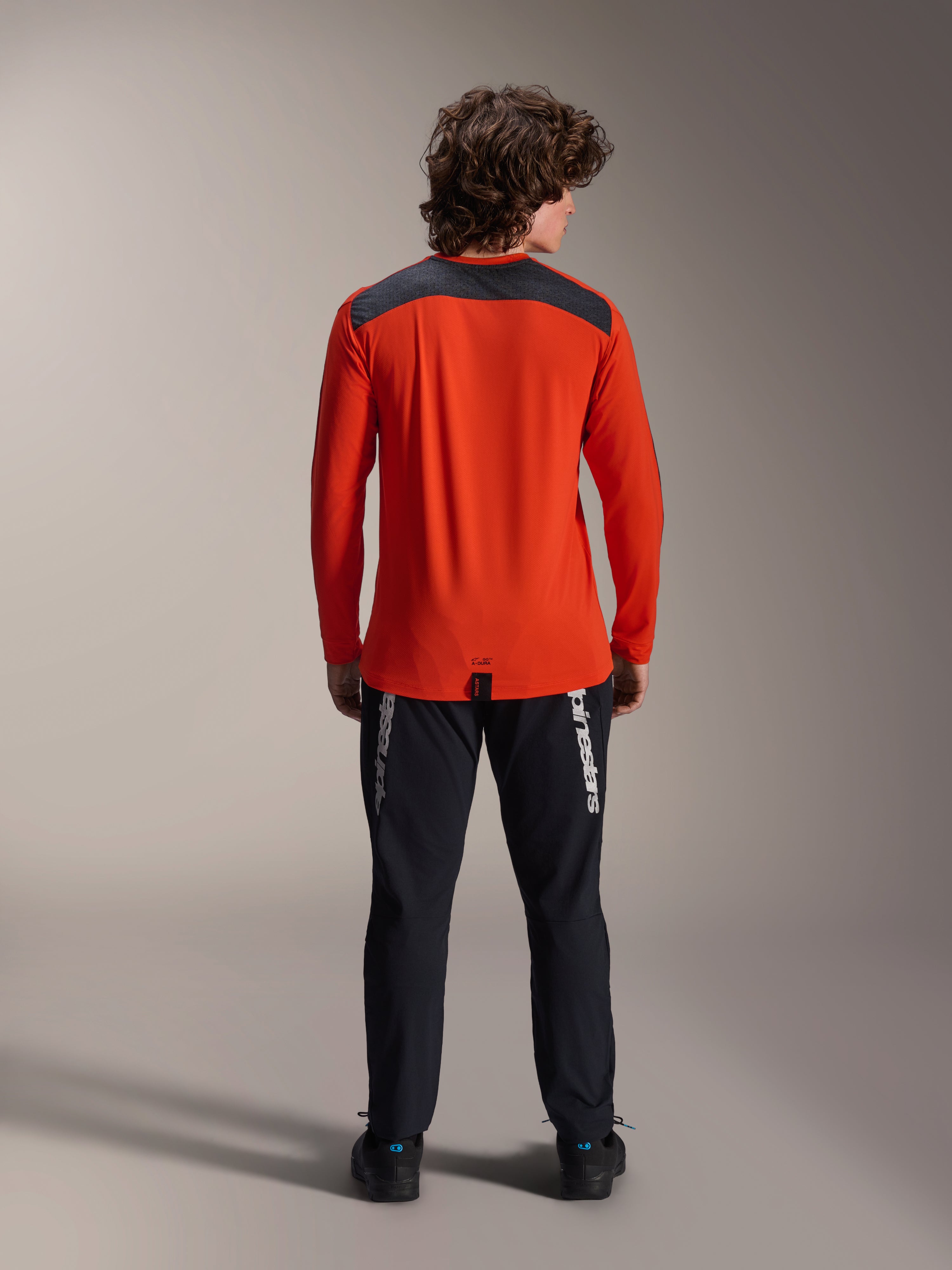 Alpinestars A-Dura Insert Astar langærmet trøje i Spicy Orange, set bagfra, koksgråt skulderpanel, kombineret med sorte Alpinestars bukser og sorte sko, professionelt studiebillede af MTB-performanceudstyr