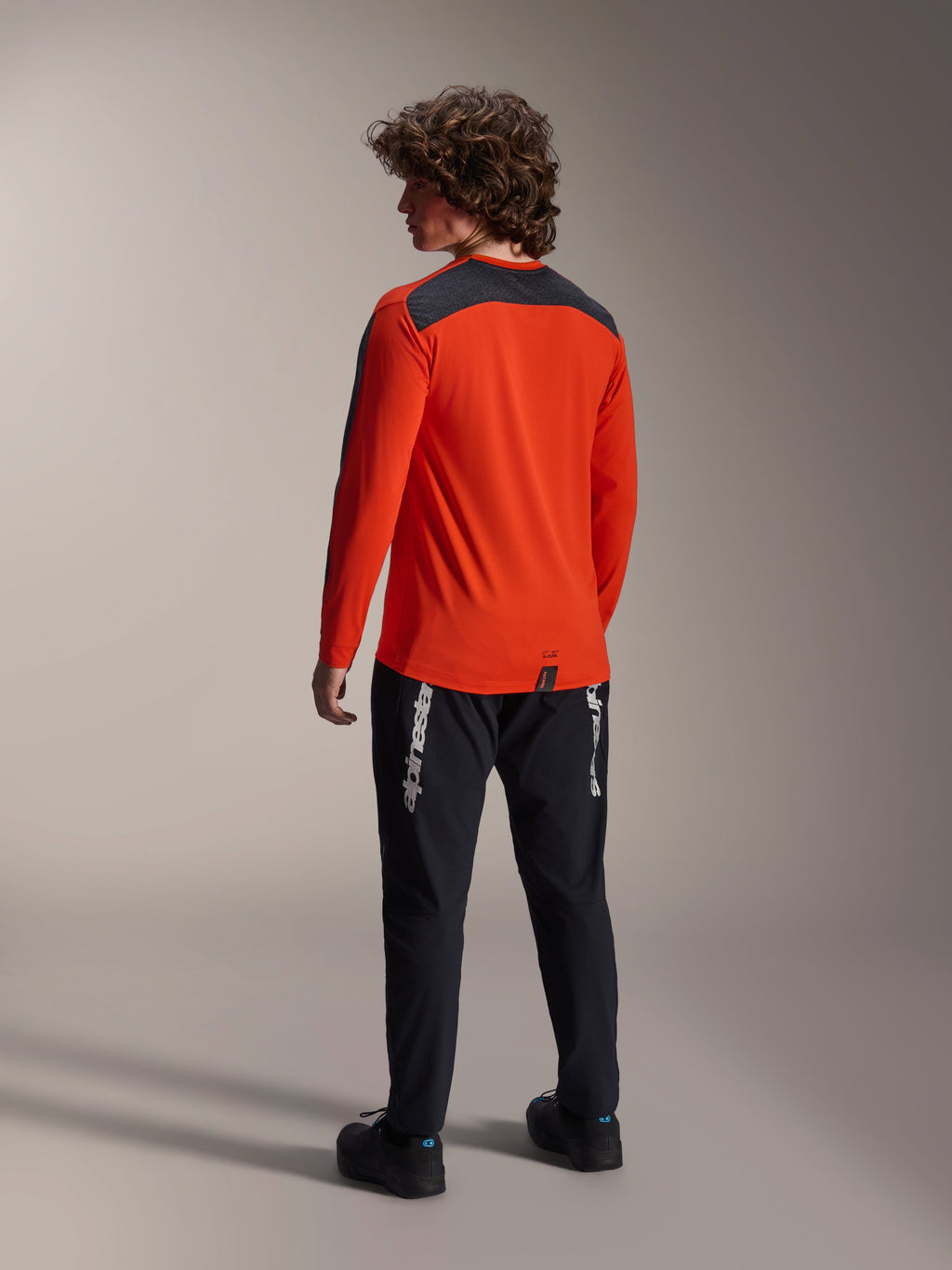 Alpinestars A-Dura Insert Astar Jersey i Spicy Orange, model set bagfra, langærmet MTB-trøje med mørkegråt skulderpanel, kombineret med sorte bukser med logo, off-road cykeludstyr.