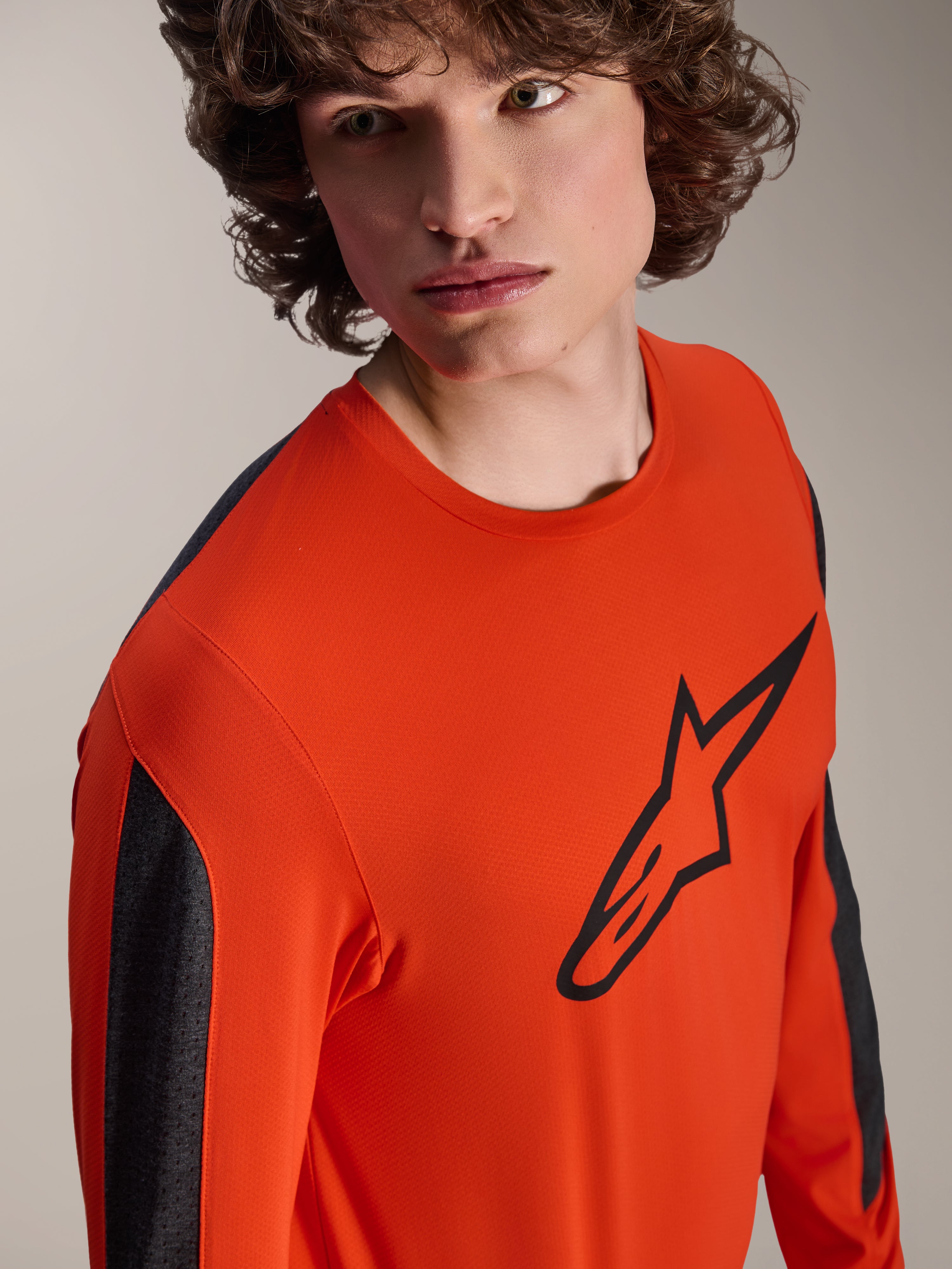 Alpinestars A-Dura Insert Astar langærmet jersey, Spicy Orange MTB-jersey med stort sort Astar-logo på brystet, mørkegrå paneler på ærmerne, båret af model i nærbillede, tekstureret teknisk materiale