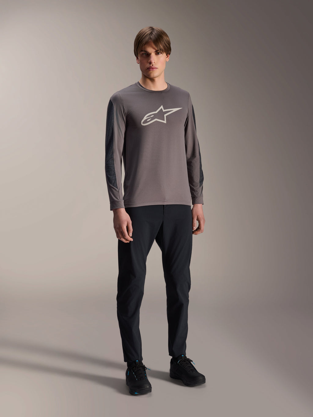 Alpinestars A-Dura Insert Astar trøje, langærmet MTB-trøje, mørkegrå, med stort hvidt brystlogo, båret med sorte tekniske bukser og sorte sko, off-road cykeludstyr