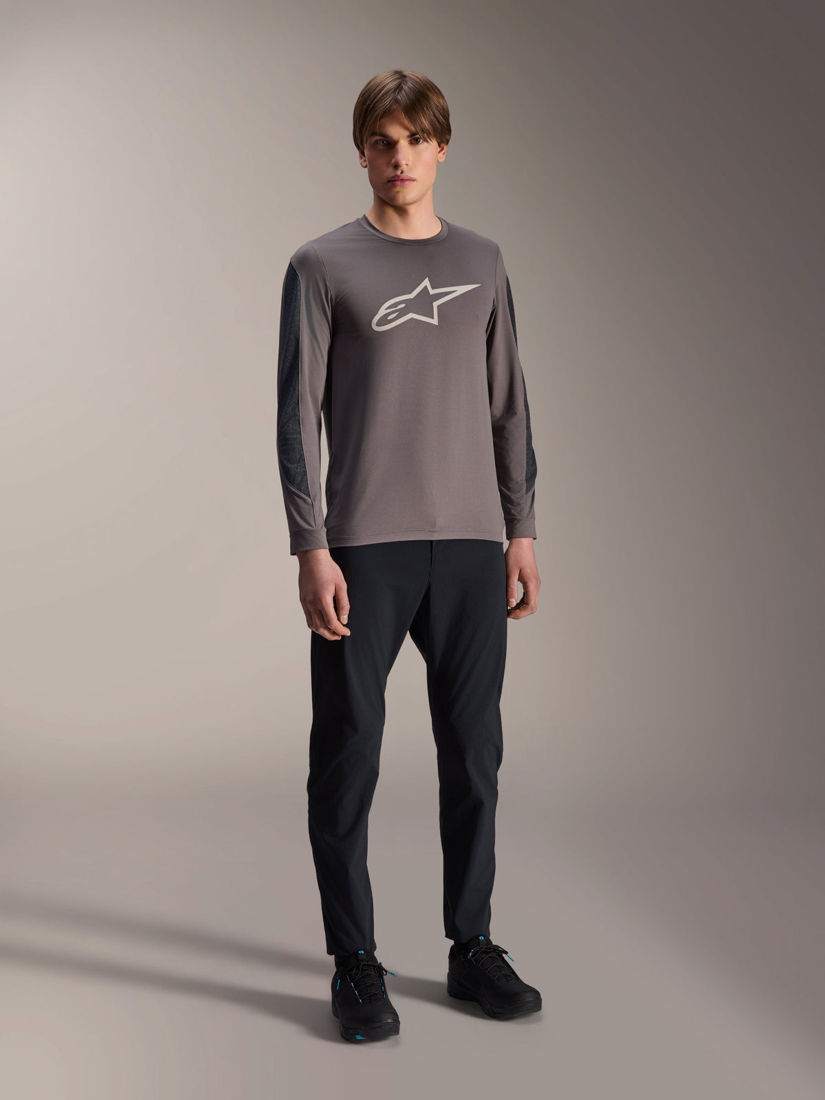 Alpinestars A-Dura Insert Astar trøje, langærmet MTB-trøje, mørkegrå, med stort hvidt brystlogo, båret med sorte tekniske bukser og sorte sko, off-road cykeludstyr
