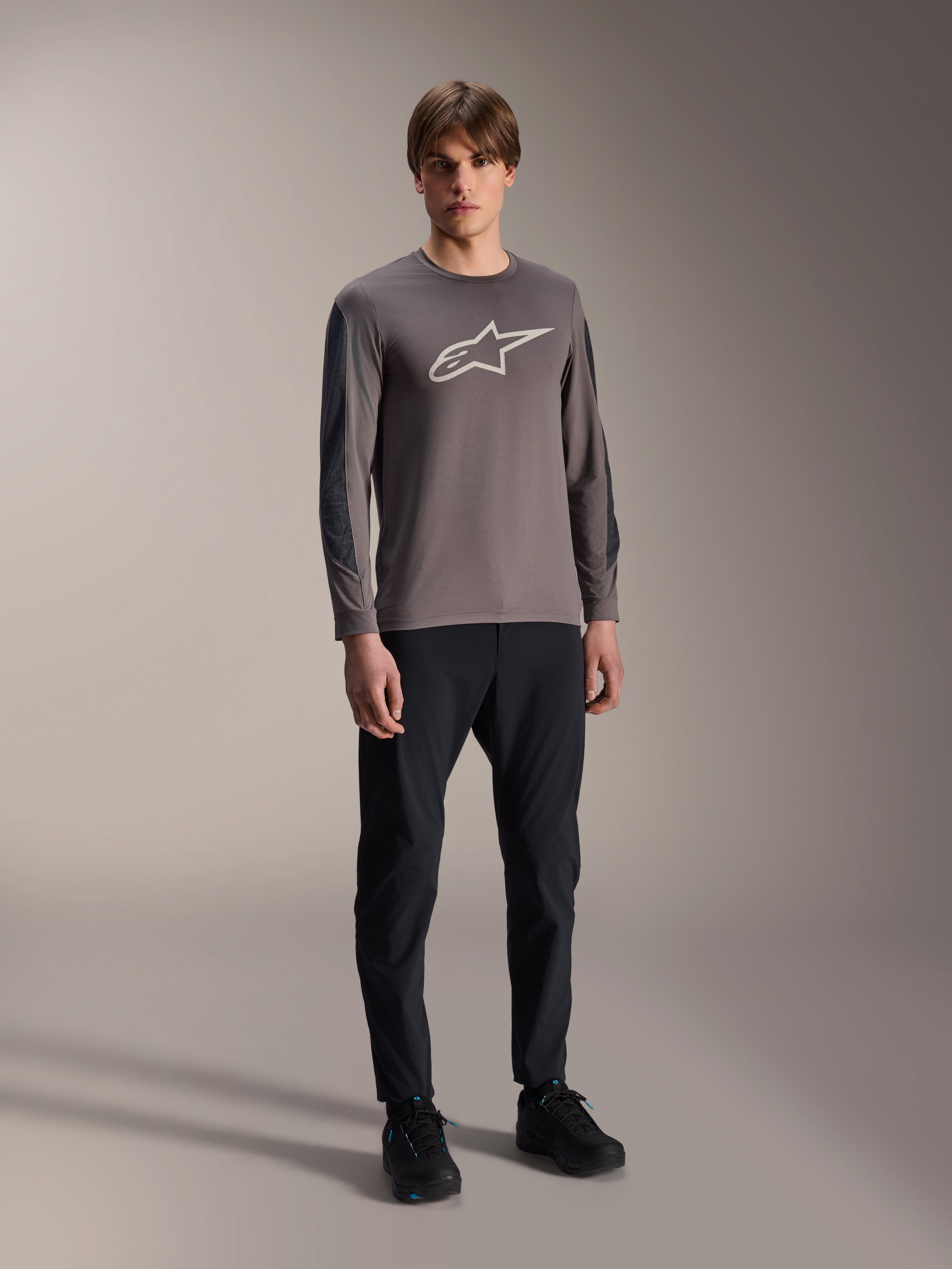 Alpinestars A-Dura Insert Astar trøje, langærmet MTB-trøje, mørkegrå, med stort hvidt brystlogo, båret med sorte tekniske bukser og sorte sko, off-road cykeludstyr