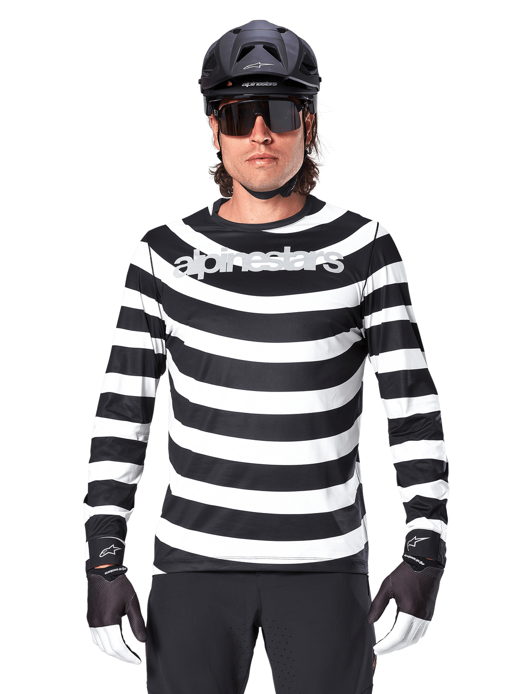 Mandlig cyklist iført Alpinestars A-Aria Oscar langærmet jersey, sorte og hvide vandrette striber, reflekterende Alpinestars-logo på brystet, stylet med sort MTB-hjelm, cykelbriller og performance-handsker