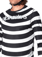 Nærbillede af Alpinestars A-Aria Oscar langærmet jersey i sort, med vandrette hvide striber, spiralformet Oscar-grafik og et reflekterende sølvfarvet Alpinestars-logo over brystet, båret af en rytter med en synlig hjelmrem.