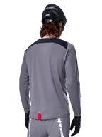 Alpinestars A-Dura Dri Astar langærmet jersey, mørkegrå MTB-trøje set bagfra, med et sort skulderpanel og lille rødt mærke, båret med en sort mountainbikehjelm og handsker.