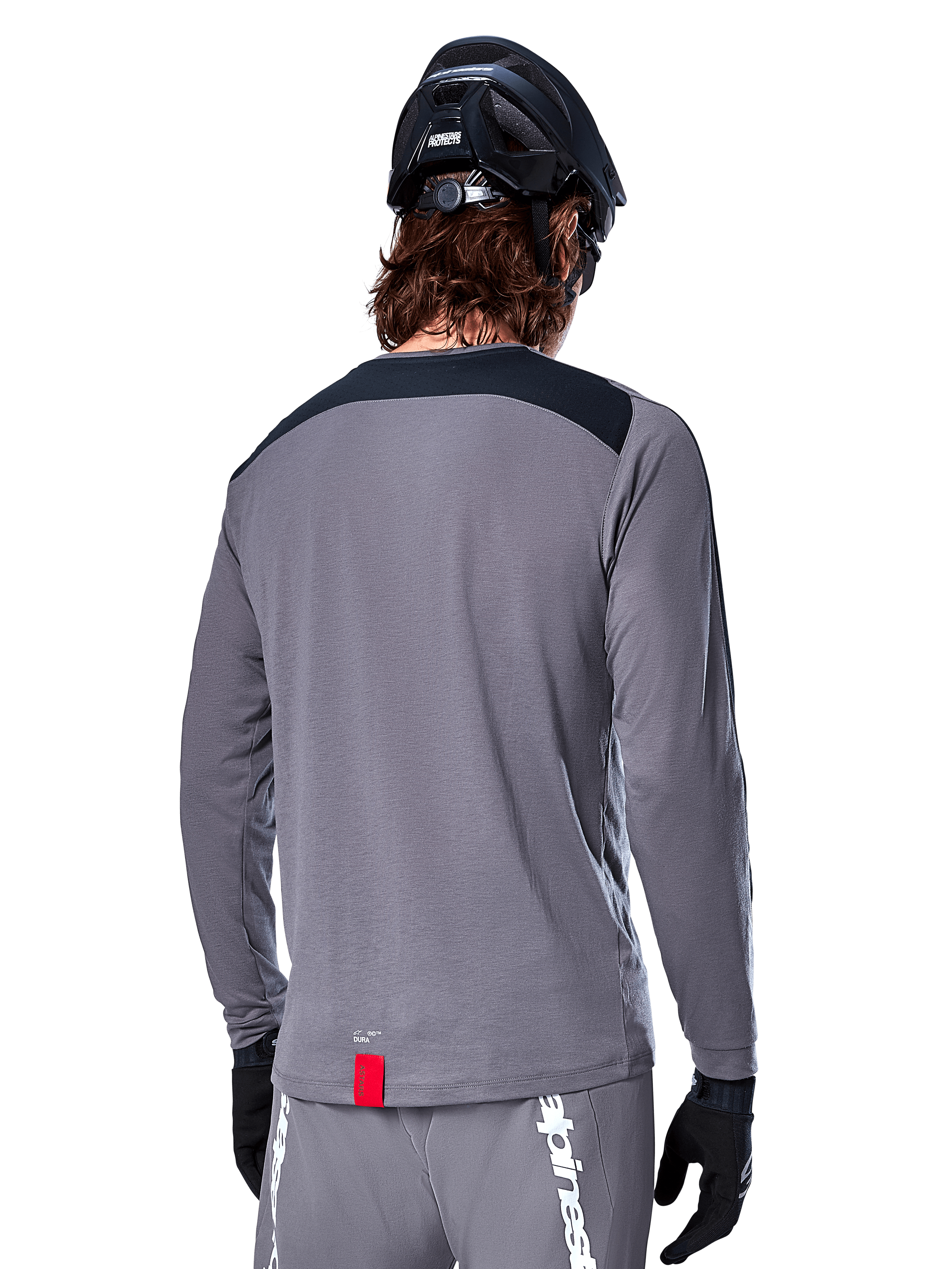 Alpinestars A-Dura Dri Astar langærmet jersey, mørkegrå MTB-trøje set bagfra, med et sort skulderpanel og lille rødt mærke, båret med en sort mountainbikehjelm og handsker.