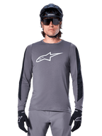 Alpinestars A-Dura Dri Astar langærmet jersey, mørkegrå, med et stort hvidt Astar-logo på brystet og sorte mesh-paneler på armene, båret af en rytter med en sort mountainbikehjelm og performance-solbriller, MTB-cykeltøj