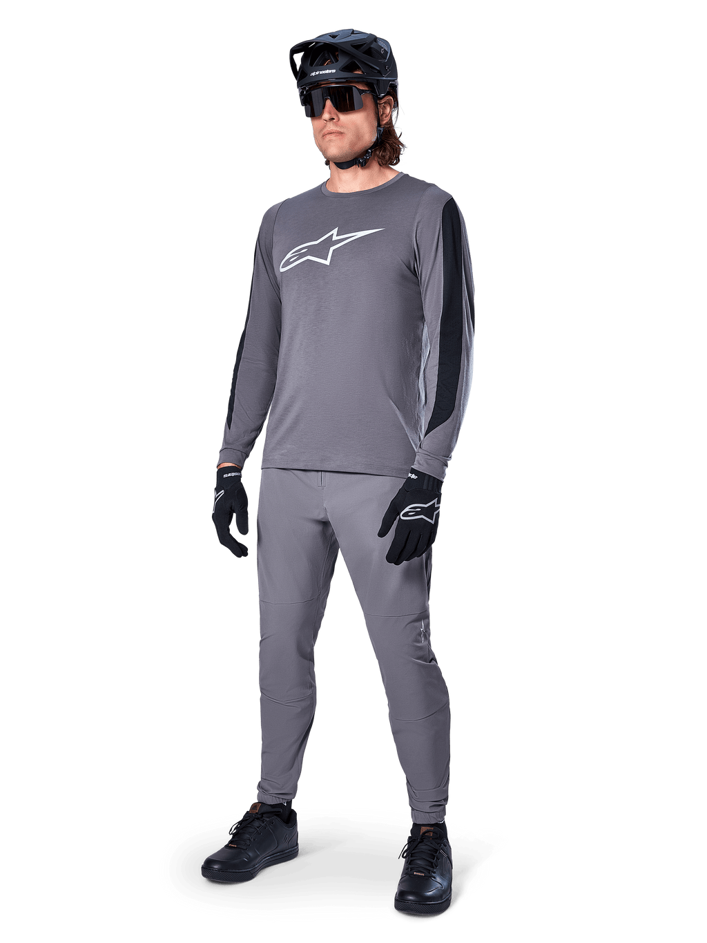 Alpinestars A-Dura Dri Astar Jersey, langærmet MTB-trøje, mørkegrå med hvidt brystlogo, sorte mesh-paneler på ærmerne, båret med matchende grå bukser, sort hjelm og handsker, performance mountainbike-tøj