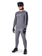 Alpinestars A-Dura Dri Astar Jersey, langærmet MTB-trøje, mørkegrå med hvidt brystlogo, sorte mesh-paneler på ærmerne, båret med matchende grå bukser, sort hjelm og handsker, performance mountainbike-tøj