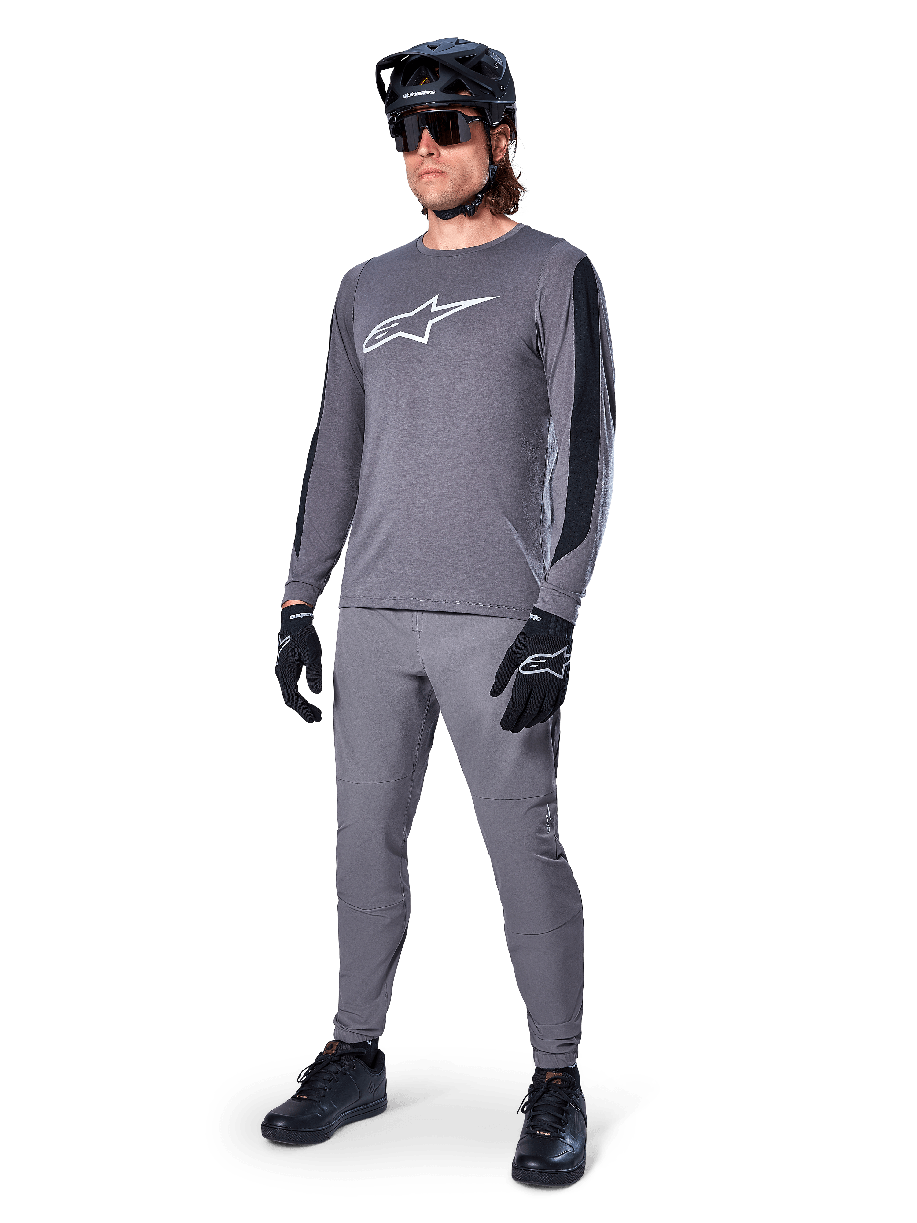 Alpinestars A-Dura Dri Astar Jersey, langærmet MTB-trøje, mørkegrå med hvidt brystlogo, sorte mesh-paneler på ærmerne, båret med matchende grå bukser, sort hjelm og handsker, performance mountainbike-tøj