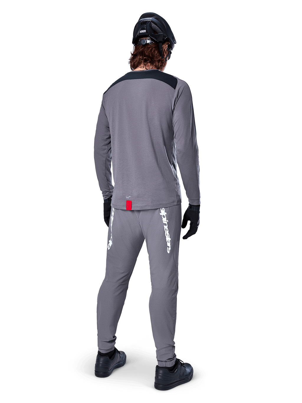 Alpinestars A-Dura Dri Astar langærmet jersey, mørkegrå, set bagfra af rytter iført matchende bukser og sort hjelm, har sorte skulderpaneler og et lille rødt mærke ved kanten, teknisk off-road cykeludstyr