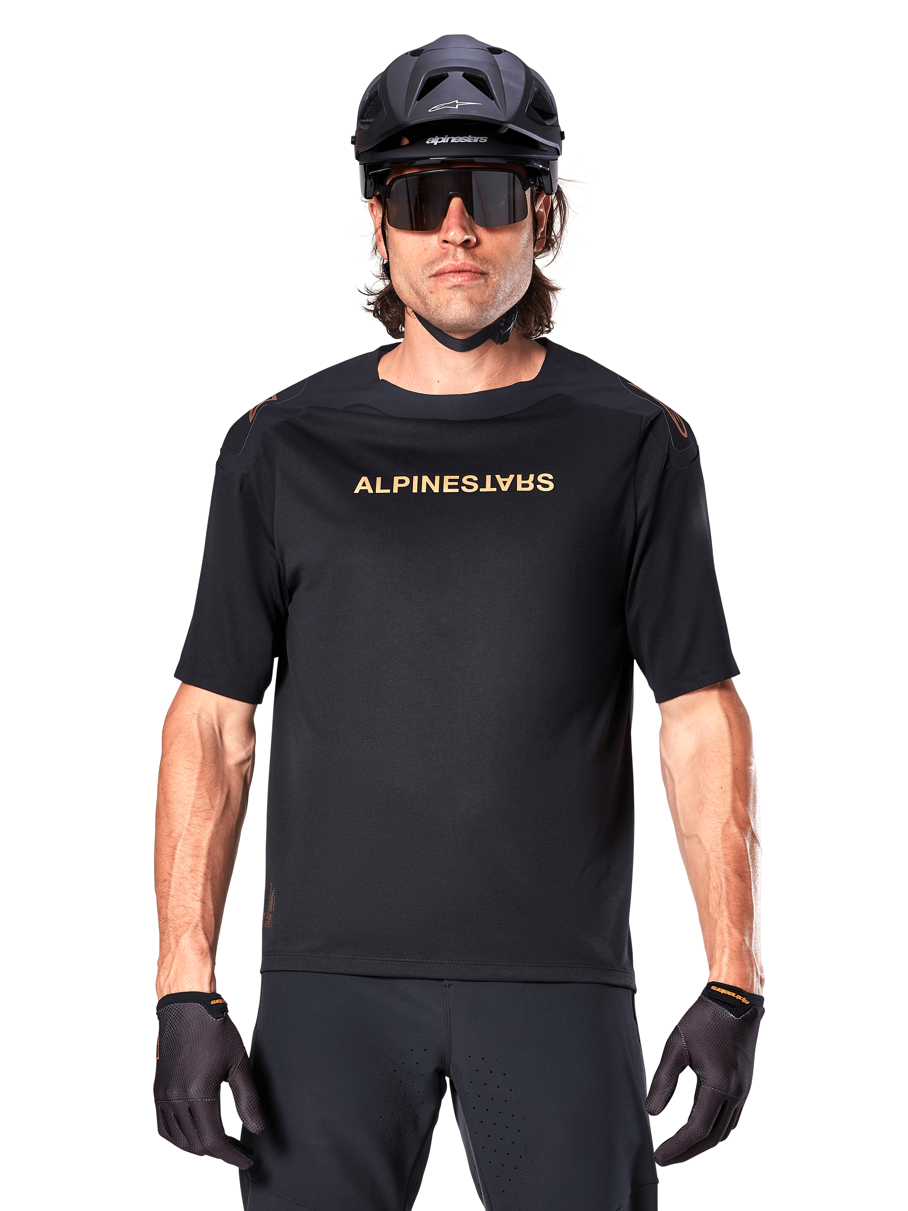 Mountainbiker iført Alpinestars A-Aria Polartec Switch kortærmet trøje i sort med guldtonet brystlogo, sort MTB-hjelm, mørke performance-solbriller og matchende handsker, off-road cykeludstyr.