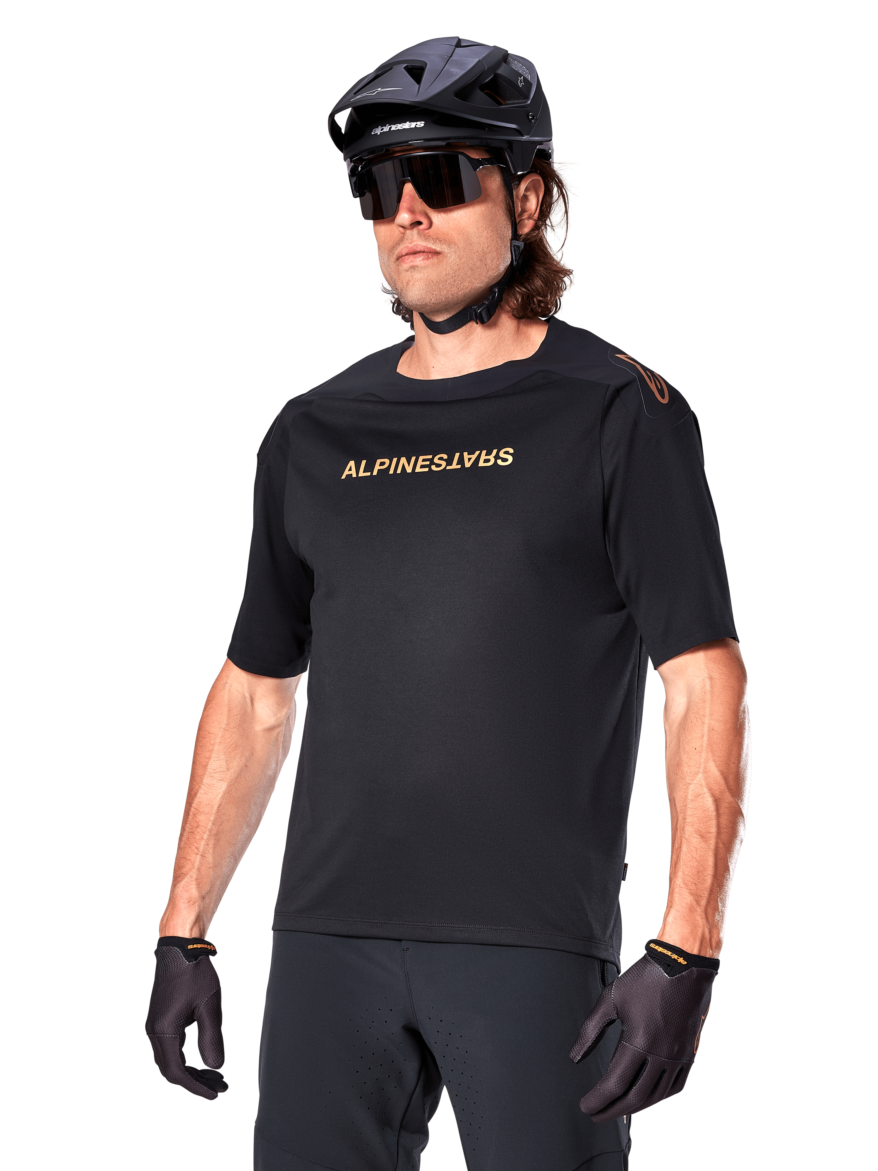 Alpinestars A-Aria Polartec Switch kortærmet cykeltrøje, sort mountainbike-trøje med guld Alpinestars-branding, sort hjelm, solbriller og handsker, teknisk MTB-beklædning