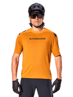 Alpinestars A-Aria Polartec Switch trøje, kortærmet, mørk guld, mountainbikerytter iført sort hjelm og solbriller, performance cykeltøj til MTB-spor