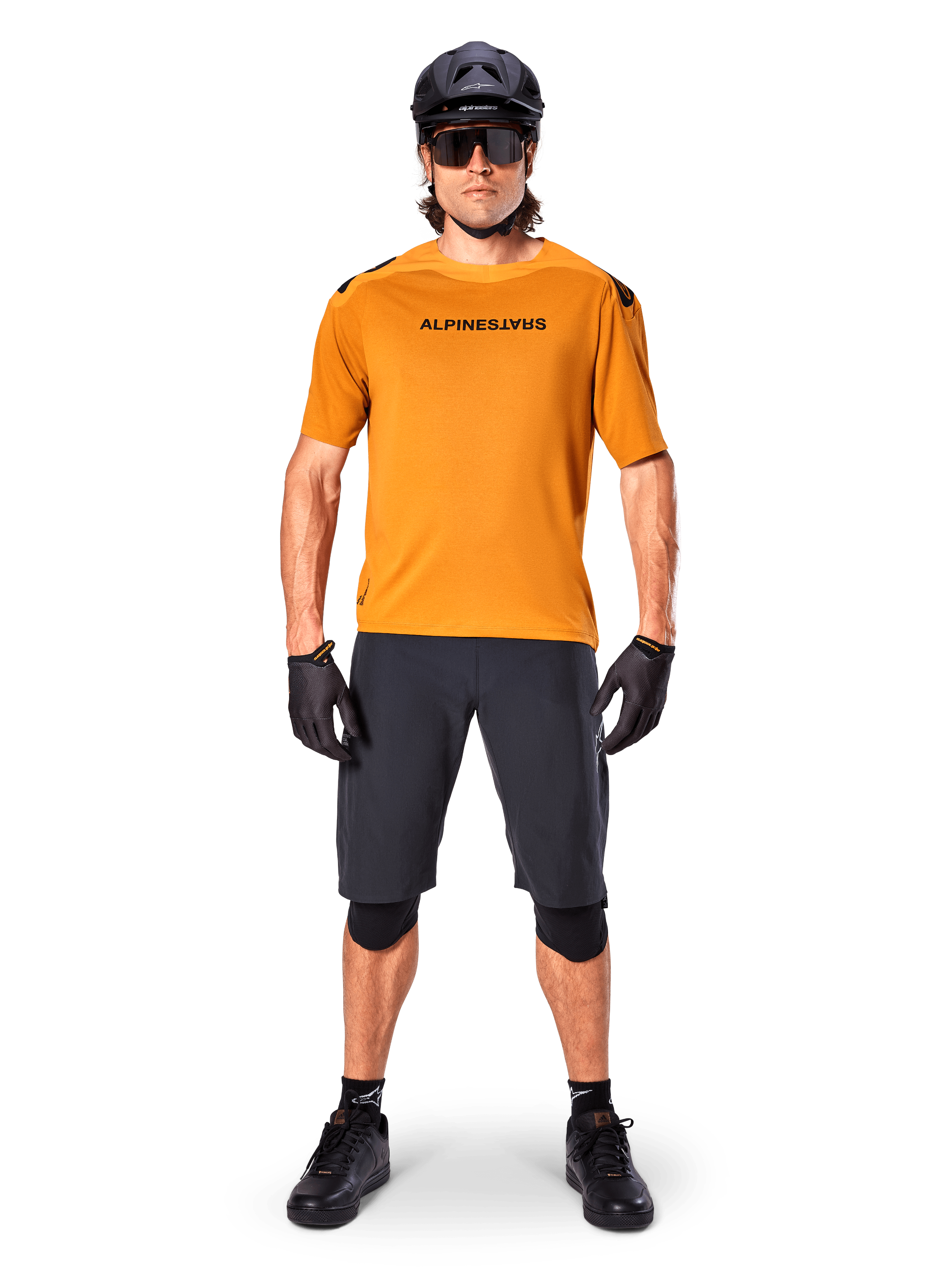 Mandlig cyklist iført Alpinestars A-Aria Polartec Switch kortærmet trøje i Dark Gold, kombineret med sorte MTB-shorts, hjelm, solbriller og handsker, professionelt mountainbike-udstyr til trailkørsel