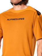 Alpinestars A-Aria Polartec Switch Jersey, kortærmet MTB-trøje, mørkt guld, med spejlvendt sort Alpinestars-logo på brystet, teknisk performance-stof til mountainbike trail-kørsel