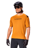 Alpinestars A-Aria Polartec Switch-trøje, kortærmet MTB-trøje, mørk guld med sort branding, båret af model med sort hjelm, solbriller og cykelhandsker, højtydende mountainbike-beklædning