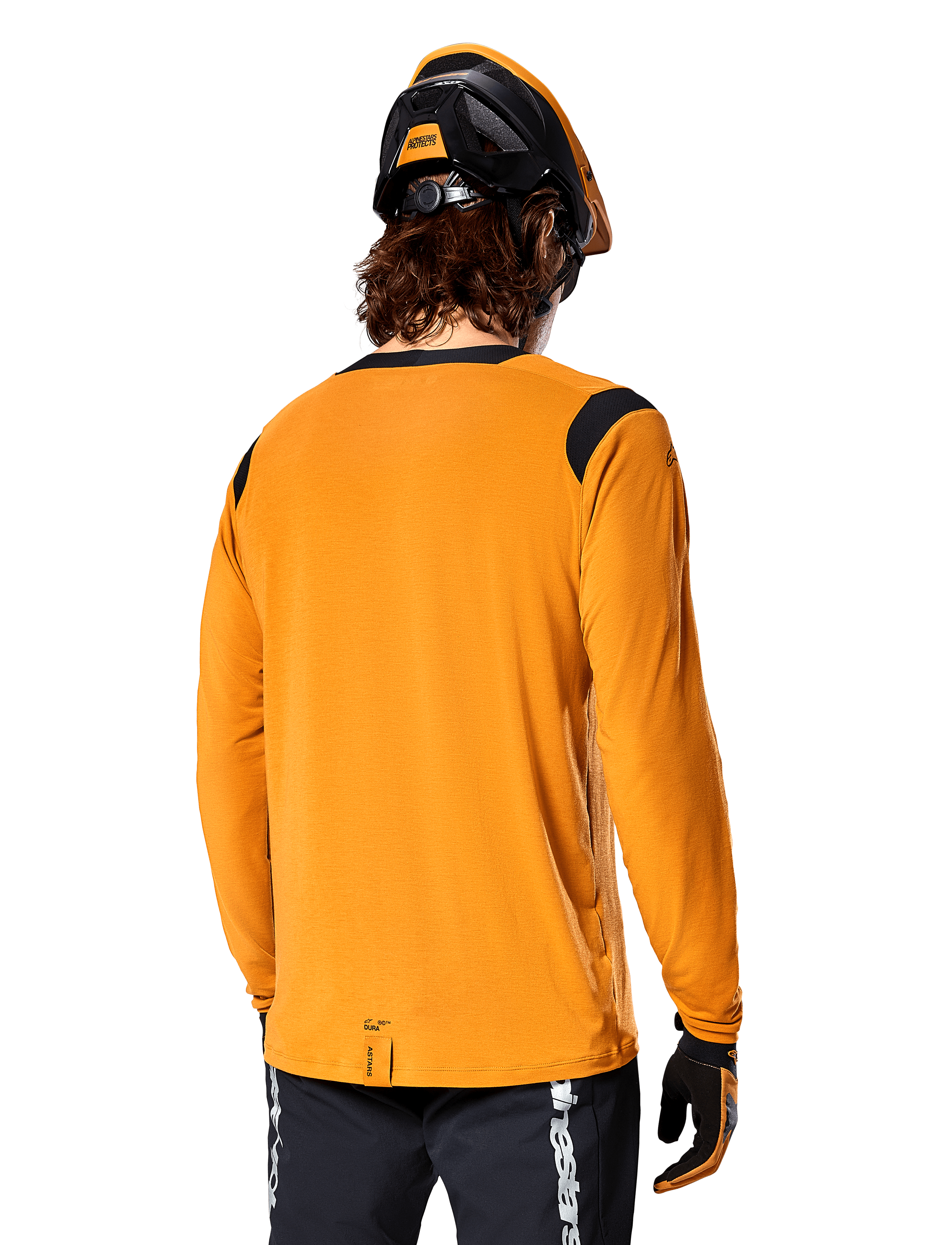 Alpinestars A-Dura Dri Wool langærmet jersey i Dark Gold, set bagfra af en rytter iført mountainbikehjelm og handsker, med sorte mesh-paneler på skuldrene og et længere rygstykke, teknisk cykeltøj til trailkørsel