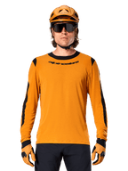 Mandlig model iført Alpinestars A-Dura Dri Wool langærmet trøje i Dark Gold, koordineret med en matchende guld MTB-hjelm og handsker, sorte mesh-paneler på skuldre og ærmer, sort Alpinestars-logo på brystet, mørke solbriller og bukser, teknisk mountainbike-beklædning