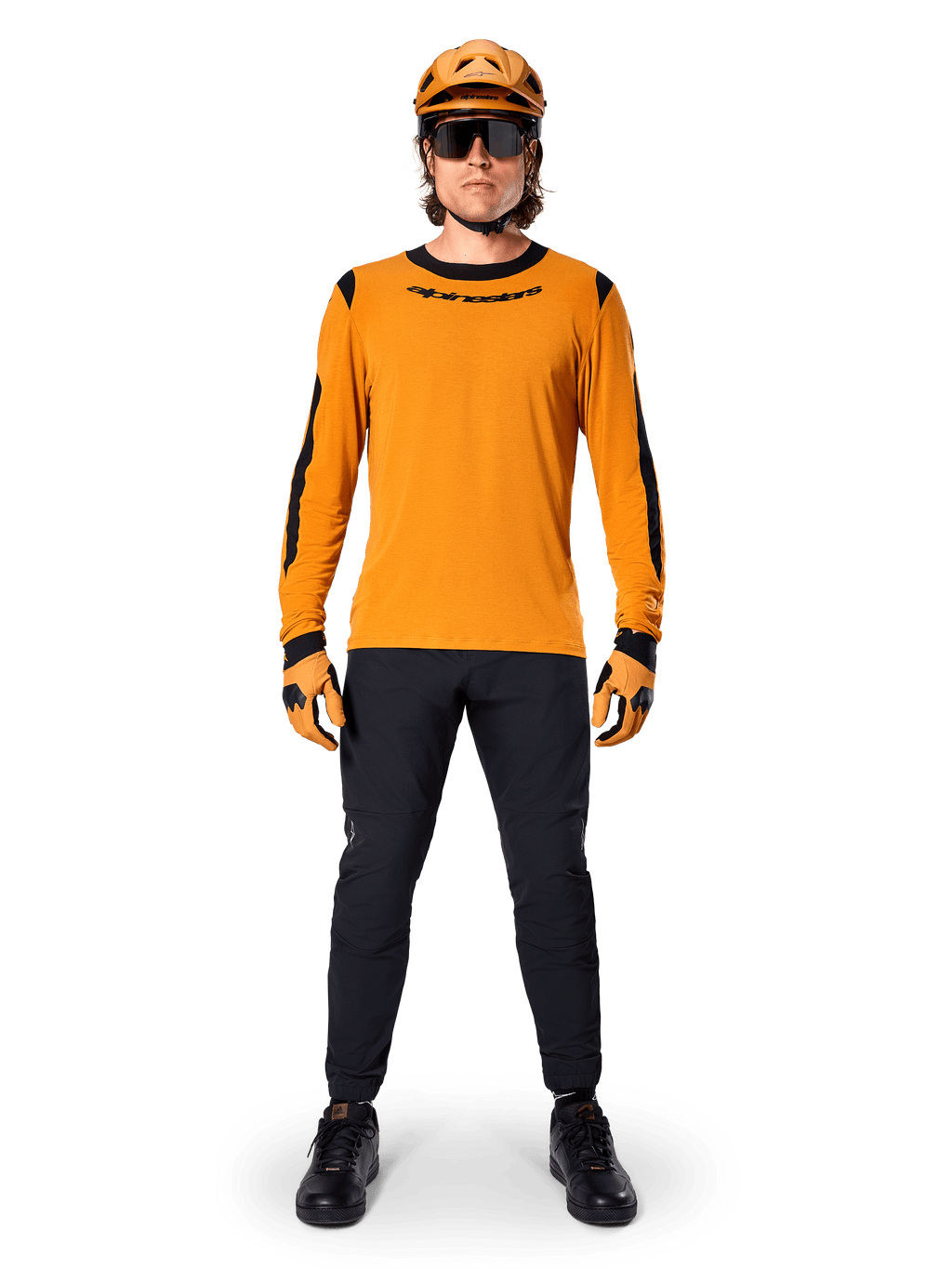 Mountainbiker iført Alpinestars A-Dura Dri Wool langærmet trøje, mørk guld med sorte detaljer på hals og ærmer, kombineret med sorte bukser, matchende guldhjelm, handsker og sorte solbriller, professionelt mountainbike-udstyr