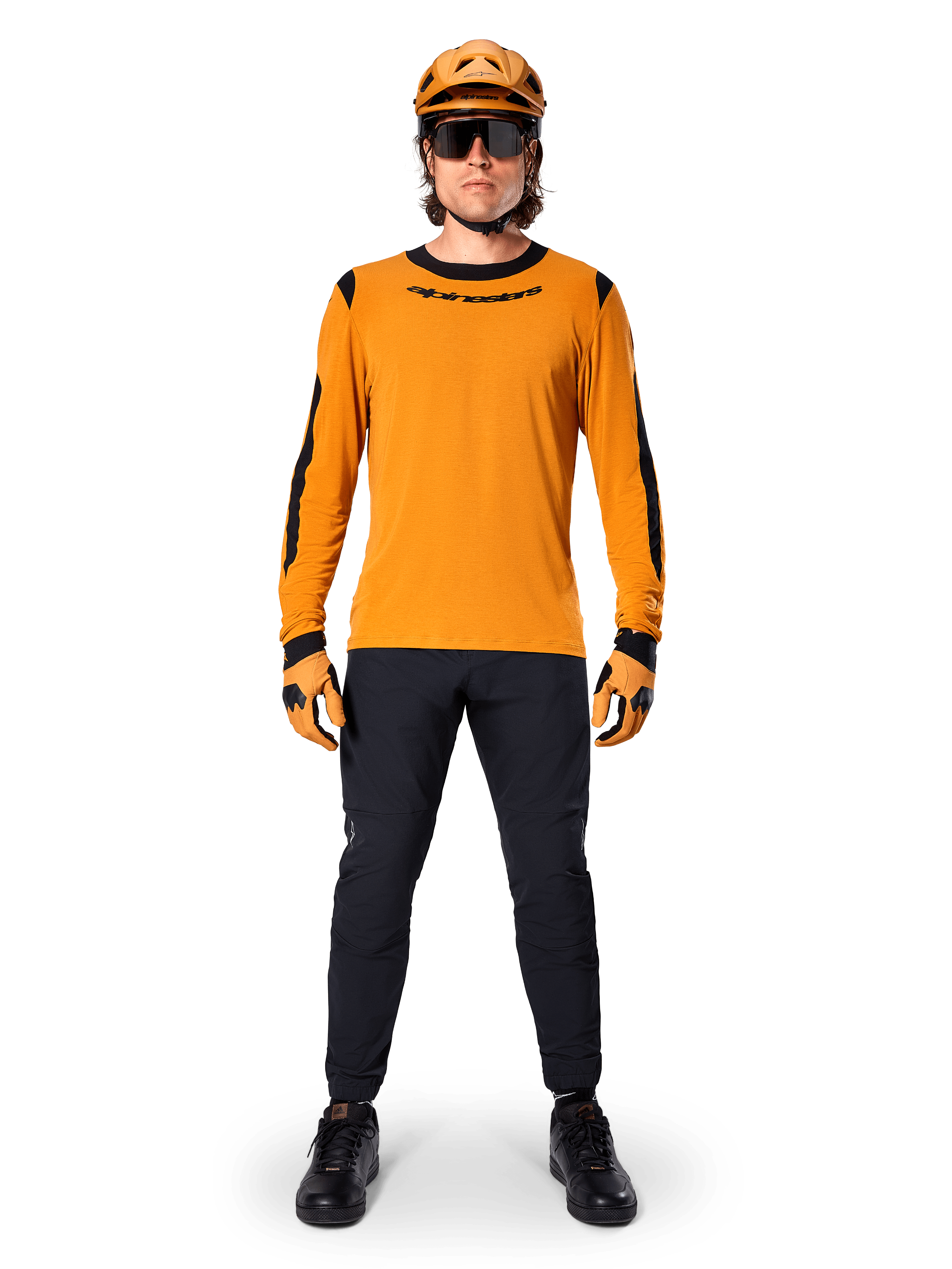 Mountainbiker iført Alpinestars A-Dura Dri Wool langærmet trøje, mørk guld med sorte detaljer på hals og ærmer, kombineret med sorte bukser, matchende guldhjelm, handsker og sorte solbriller, professionelt mountainbike-udstyr