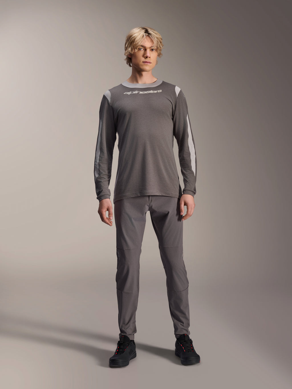 Alpinestars A-Dura Dri Wool langærmet trøje, mørkegrå, båret af model med matchende grå bukser og sorte sko, hvidt Alpinestars-logo på brystet, lysegrå mesh-paneler på skuldre og ærmer, teknisk mountainbike-udstyr