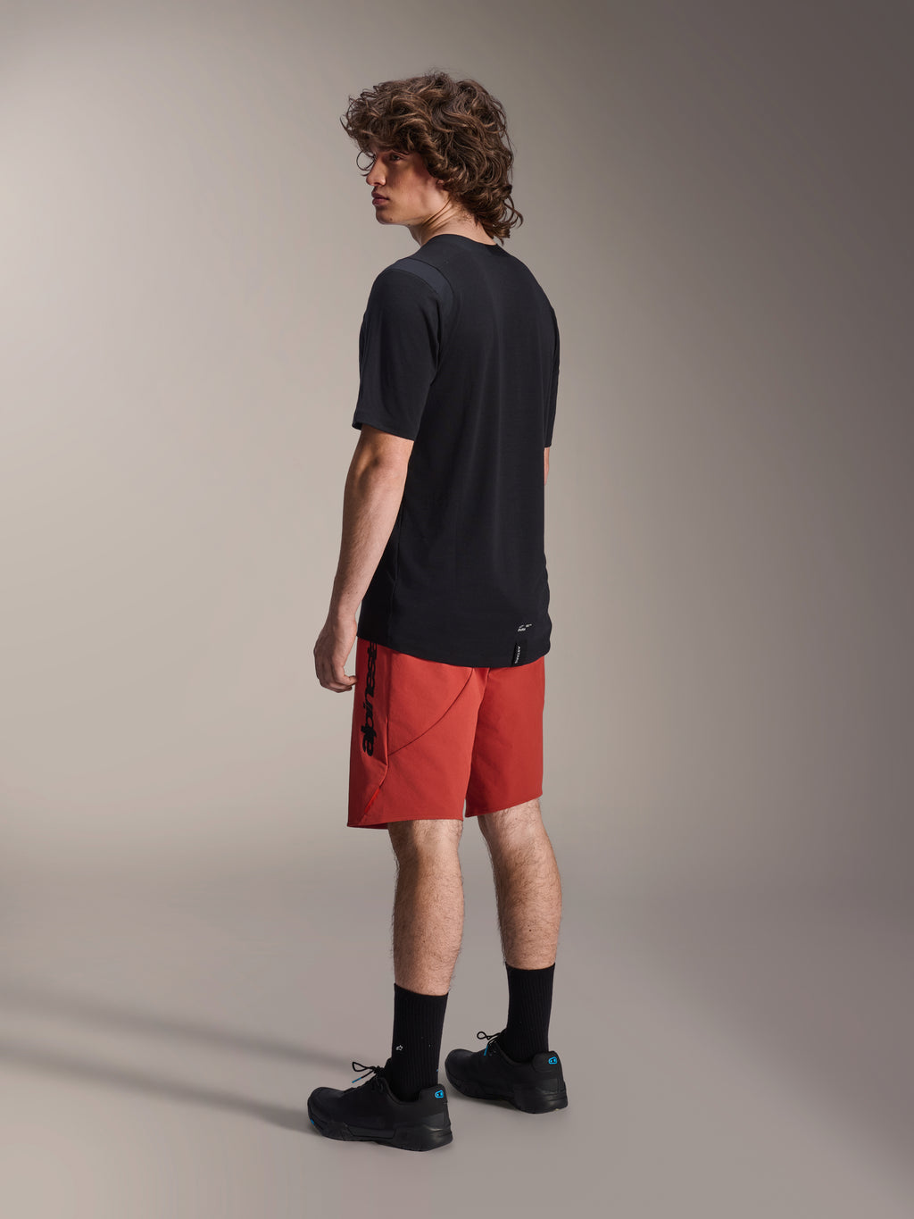 Alpinestars A-Dura Elite shorts, mountainbike-shorts, mørkorange, båret med en sort kortærmet trøje og sorte mountainbike-sko, set bagfra fra siden af model, der fremhæver performance-pasform og branding