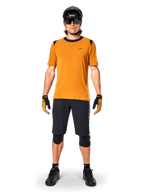 Alpinestars A-Dura Dri Wool Short Sleeve Jersey in Dark Gold, mountain bike jersey worn with black shorts and protective gear, mustard yellow fabric with black collar and shoulder accents, performance cycling apparel for trail riding.