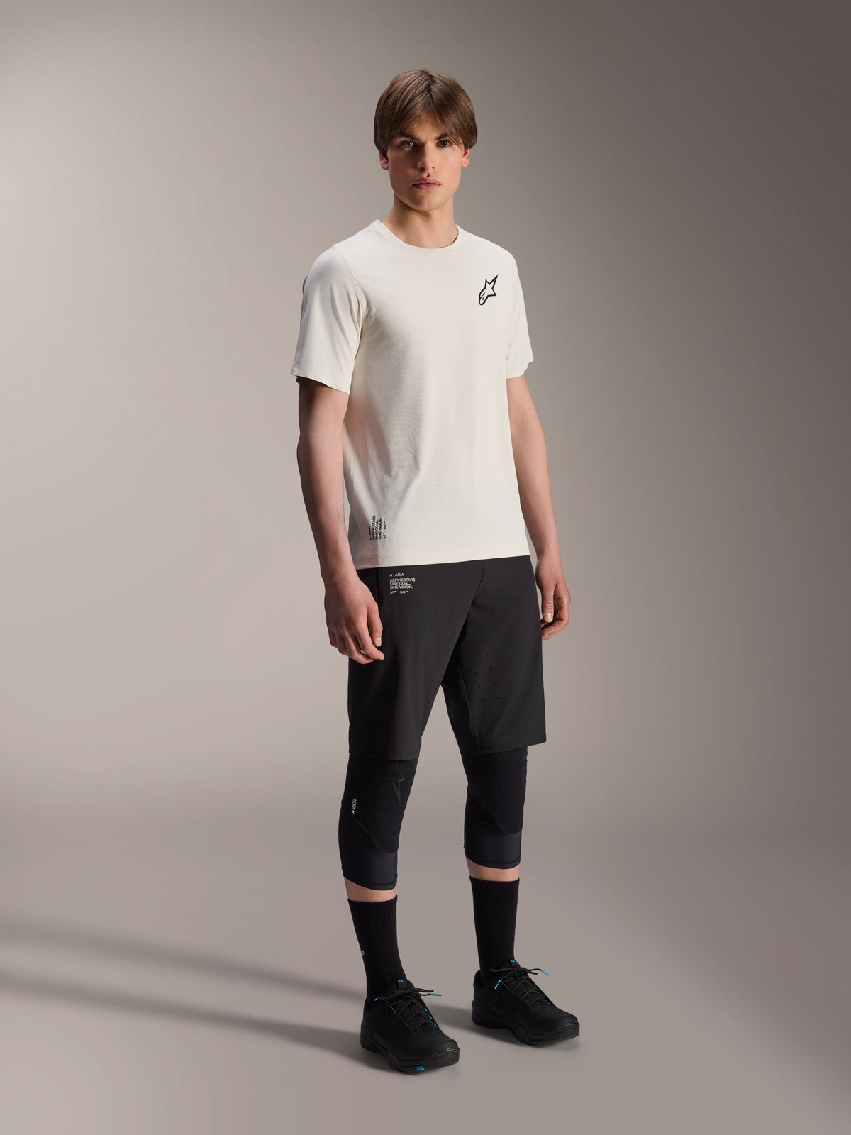 Alpinestars A-Aria Astar trøje, kortærmet, Ecru, med sort logo på brystet, båret med sorte cykelshorts og knæbeskyttere, letvægts MTB-performanceudstyr