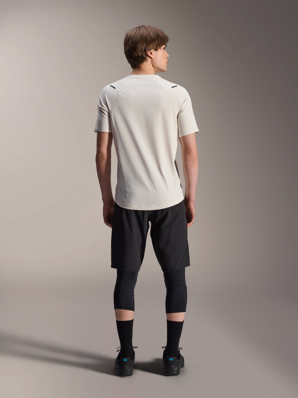 Mandlig model set bagfra iført Alpinestars A-Aria Astar kortærmet trøje i Ecru, kombineret med sorte MTB-shorts og beskyttende leggings, med forlænget bagstykke og performance fit til off-road trailkørsel.