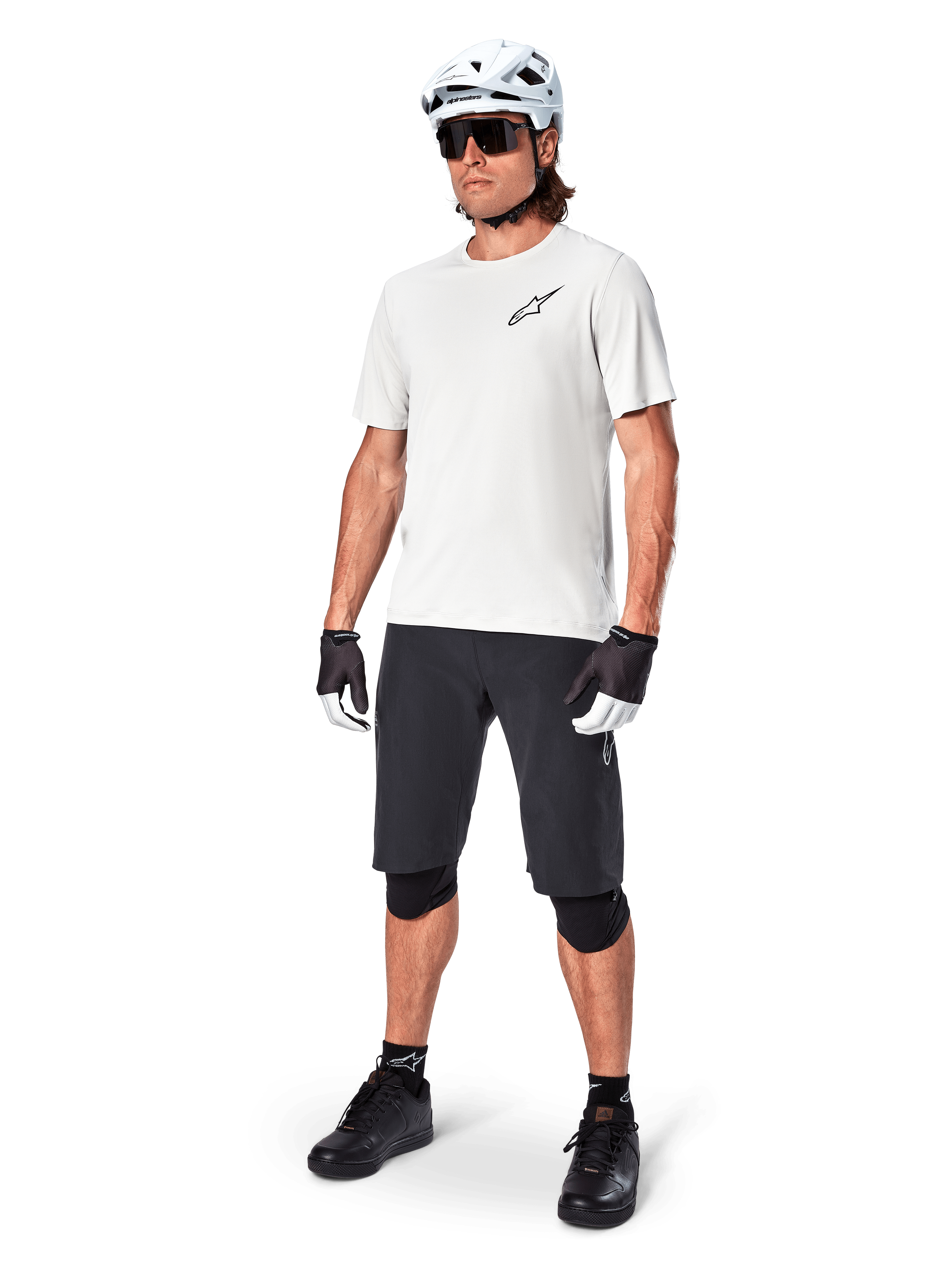 MTB rider wearing Alpinestars A-Aria Astar Short Sleeve Jersey in White Dove, paired with black mountain bike shorts, white helmet, and black knee guards, featuring a small black logo on the chest, coordinated cycling gear for trail performance