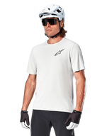 Alpinestars A-Aria Astar Short Sleeve Jersey, White Dove, worn by a cyclist with a white helmet and dark sunglasses, featuring a small black star logo on the chest, breathable performance gear for mountain biking