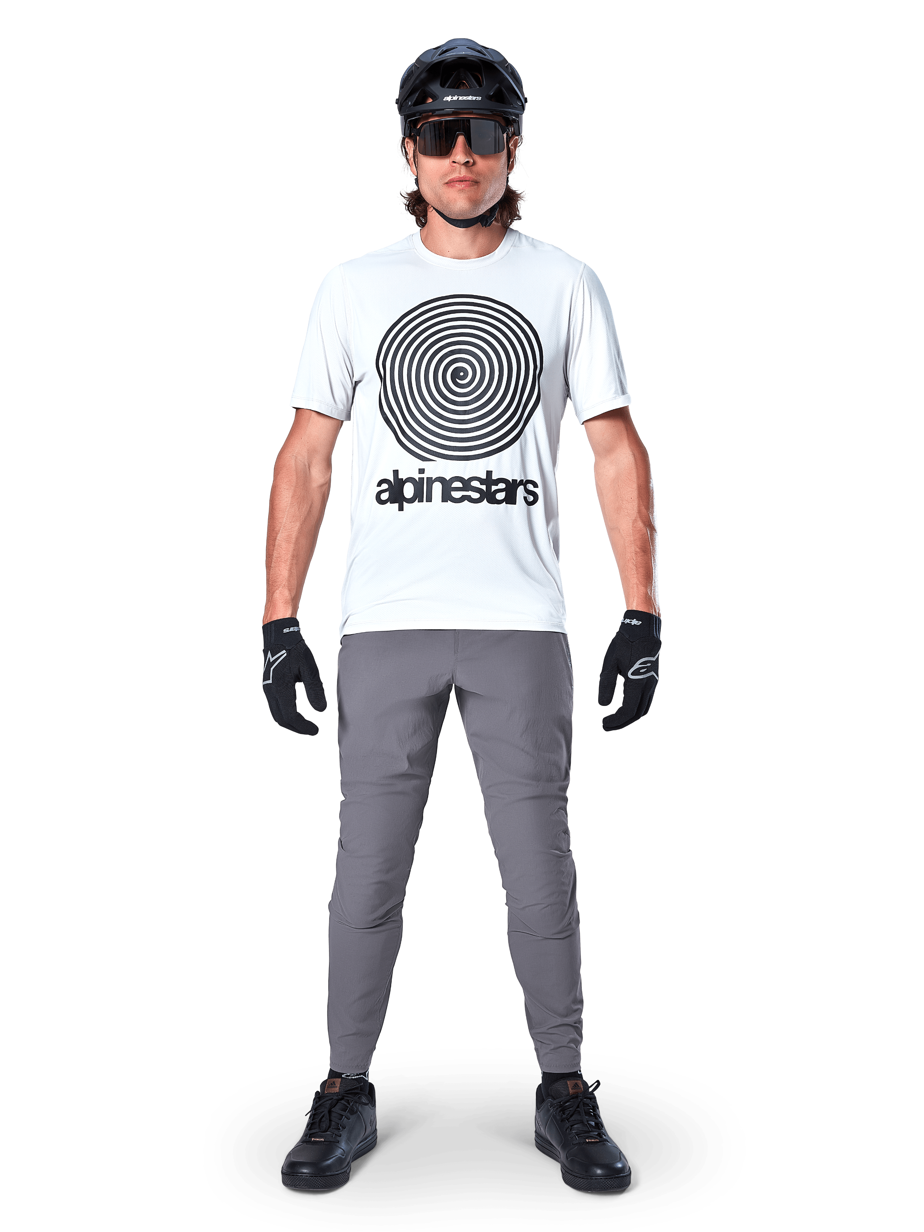 Mountain biker wearing Alpinestars A-Dura Oscar Jersey, Short Sleeve, White Dove with large black spiral logo, paired with grey pants, black helmet, sunglasses, and black gloves, performance MTB trail riding gear