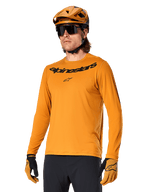 Alpinestars A-Dura Rocker Long Sleeve Jersey, MTB Mountain Biking Jersey, Dark Gold, person wearing jersey with matching helmet and gloves, sporty coordinated look with Alpinestars wordmark on chest