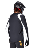 MTB-rytter iført Alpinestars A-Supra Oscar langærmet trøje, sort med hvide paneler på skuldre og ærmer, set bagfra, sort hjelm og handsker, bukser med orange detaljer, holdbart off-road cykeltøj