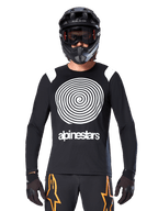 Alpinestars A-Supra Oscar langærmet jersey, sort med hvid spiralgrafik og skulderdetaljer, båret af en rytter med sort full-face hjelm og goggles, sorte og orange bukser, performance cykeludstyr til MTB gravity-kørsel