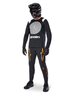 MTB-rytter iført Alpinestars A-Supra Oscar langærmet trøje i sort med hvid vintage Oscar-spiralgrafik, sorte bukser med orange stjernelogoer, sort full-face hjelm med goggles og sorte handsker, professionelt mountainbike-udstyr