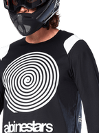 Alpinestars A-Supra Oscar Jersey, langærmet, sort, med en stor hvid Oscar-spiralgrafik på brystet og brand-logo, båret af en rytter med en sort full-face hjelm og goggles, performance mountainbike-tøj til gravity-kørsel